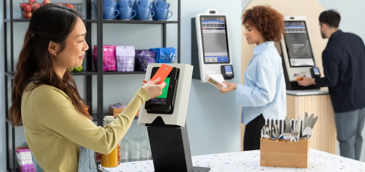 Customers using touchscreen self-checkout kiosks beside stocked micro market shelves